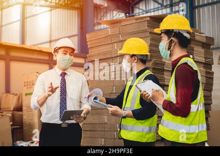 Factory warehouse manager speak with Asian worker working together with safety and face mask Stock Photo