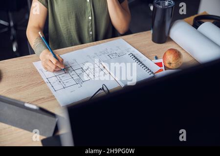 Close up shot of hand of female interior designer making notes on a blueprint, sitting at the table in her office Stock Photo