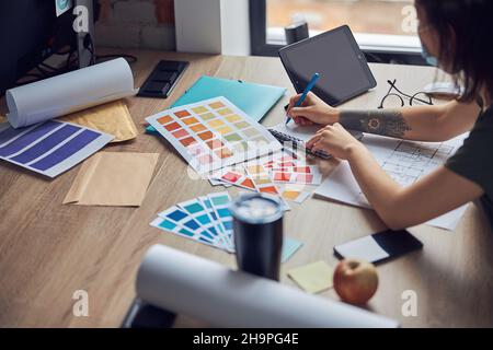 Close up shot of working process of interior designer making notes in her notebook, selecting color samples, sitting at the table in her office Stock Photo