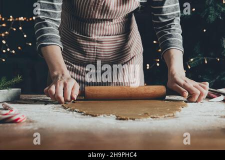 Merry Christmas, Happy New Year. Gingerbread cooking, cake or strudel baking. A young woman or mother rolls out the dough with a rocking chair for extruding and cutting out cookies. High quality photo Stock Photo