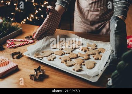 Merry Christmas, Happy New Year. Gingerbread cooking, cake or strudel baking. A young woman or mother holds deco, holding sheet with ready-made baked cookies in her gloves hands. High quality photo Stock Photo