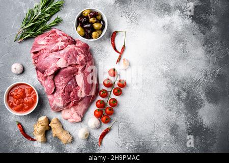 Raw lamb shoulder meat ready for baking, with ingredients and herbs, on gray stone table background, top view flat lay, with copy space for text Stock Photo