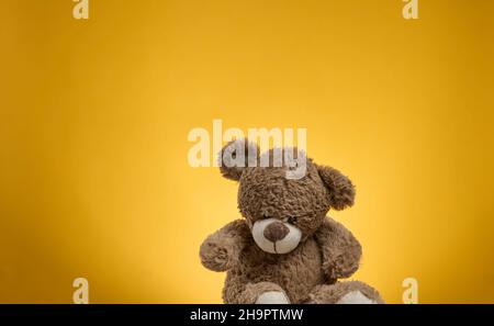 cute brown teddy bear with patches sits on a yellow background, childrens toy Stock Photo