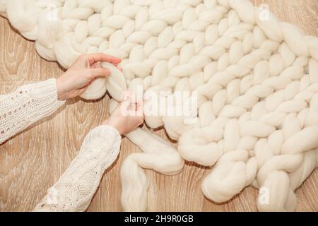 Women's hands knit a plaid of merino wool of large knitting on a wooden floor, top view flat lay. Master class step by step, training Stock Photo