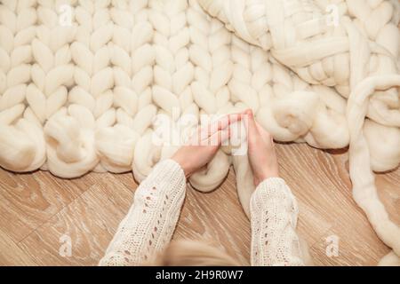 Women's hands knit a plaid of merino wool of large knitting on a wooden floor, top view flat lay. Master class step by step, training Stock Photo