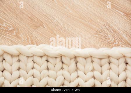 Knitted plaid of large knitting made of merino wool on wooden floor. Stock Photo