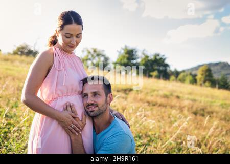 Proud husband with her pregnant wife. Young maried couple outdoors Stock Photo