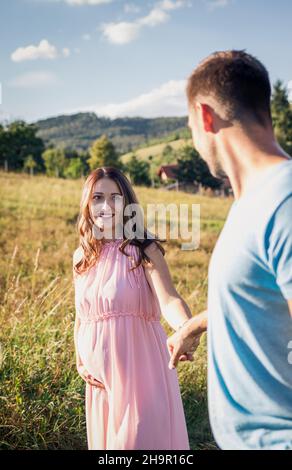 Happy couple expecting baby holding hands. Smiling pregnant woman following her husband Stock Photo