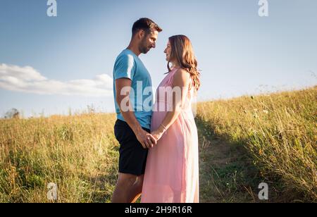 Young couple expecting baby. Parents holding hands together and standing in meadow Stock Photo