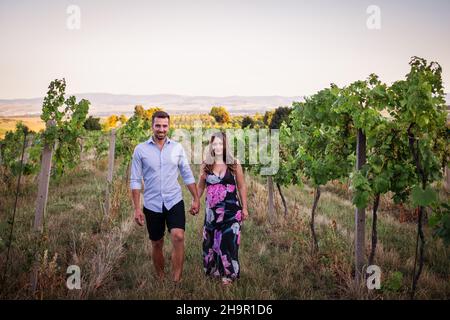 Young couple walking in vineyard. Handsome man with her beautiful pregnant woman outdoors. Happy married people Stock Photo