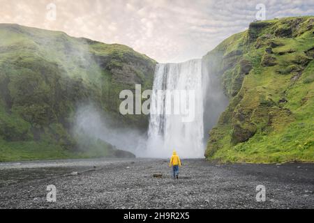 Huge waterfall behind a person, Skogafoss waterfall, South Iceland, Iceland Stock Photo