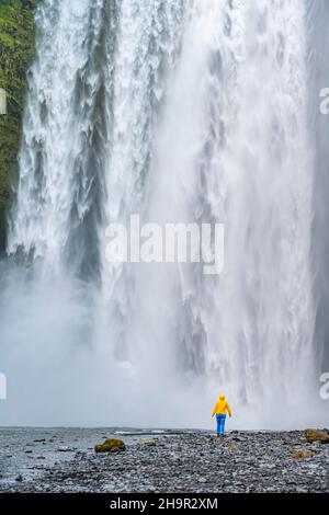 Huge waterfall behind a person, Skogafoss waterfall, South Iceland, Iceland Stock Photo