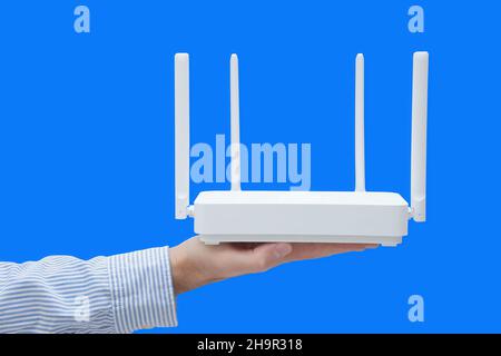 Close-up of a businessman's hand holding a wi-fi router against a blue background. Wireless networking in the office. Stock Photo