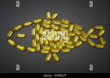 Omega-3 fish oil softgels arranged into a fish symbol on a black background. Fatty acids dietary supplement. Stock Photo