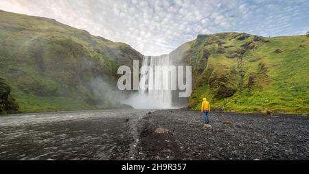 Huge waterfall behind a person, Skogafoss waterfall, South Iceland, Iceland Stock Photo