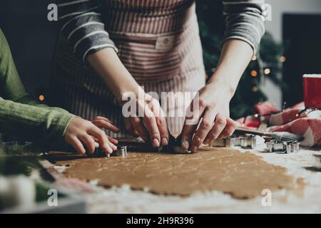 Merry Christmas, Happy New Year. Gingerbread cooking, baking. Mom and daughter make cookies, cut out different shapes of cookies using cutting metal mold on wooden table at kitchen. High quality photo Stock Photo