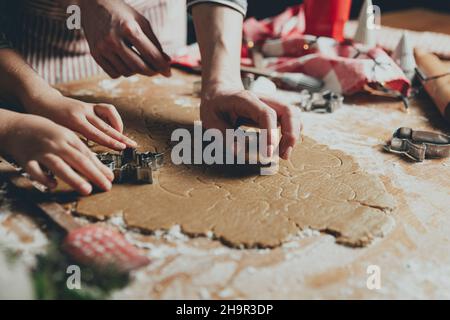 Merry Christmas, Happy New Year. Gingerbread cooking, baking. Mom and daughter make cookies, cut out different shapes of cookies using cutting metal mold on wooden table at kitchen. High quality photo Stock Photo