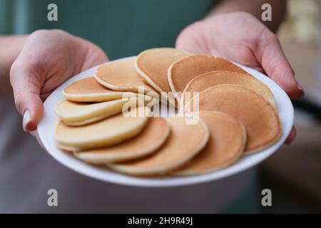 Round appetizing flour pancakes on white plate in female hands Stock Photo