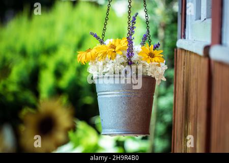 Hanging flower pot with colorful flowers. Decoration in ornamental garden at summer. Bouquet of white hydrangea, heliopsis (false sunflower) Stock Photo