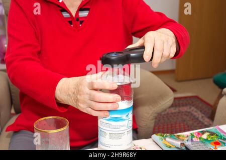 Old woman, senior citizen, 84 years, opening a water bottle with an opener for seniors, Munich, Bavaria, Germany Stock Photo