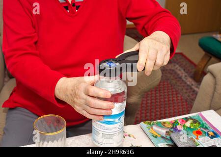 Old woman, senior citizen, 84 years, opening a water bottle with an opener for seniors, Munich, Bavaria, Germany Stock Photo