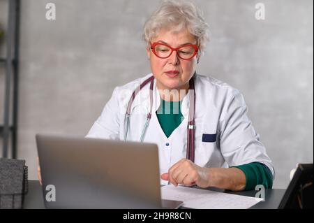 Middle age female doctor using laptop, writing notes with stethoscope on table. Healthcare concept. Medical doctor writing and taking notes Stock Photo