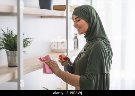 Muslim young woman cleaning shelfs with detergent at home Stock Photo