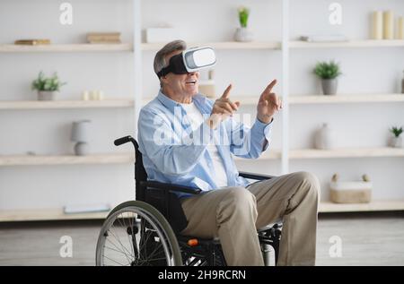 Happy senior man in wheelchair using VR headset to explore augmented reality at home Stock Photo