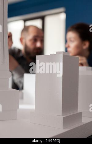 Closeup of white foam architectural scale model of residential building complex in front of architects team working together. Detail of urban development project on design table. Stock Photo
