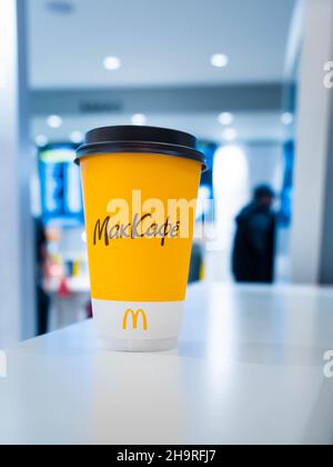 Moscow, Russia - April 3, 2021: One yellow cup of coffee on the table at Mcdonalds, people stand at the customer service counter on background. The Stock Photo