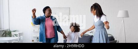 excited african american kid dancing in living room with mom and granny, banner Stock Photo