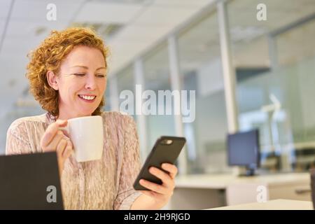 Young businesswoman reads a text message on the smartphone and drinks a cup of coffee Stock Photo