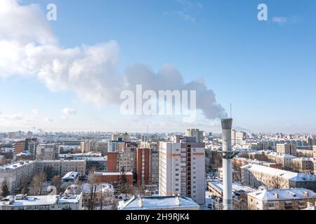 smoking pipe of thermal power plant against blue sky and cityscape in winter time. aerial photography. Stock Photo