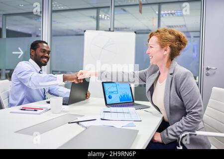 Two business colleagues at the desk having a fist bump as a symbol for motivation Stock Photo