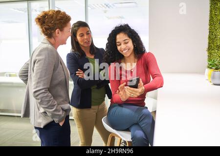 Group of women having a break in the office on the smartphone has fun reading a text message Stock Photo