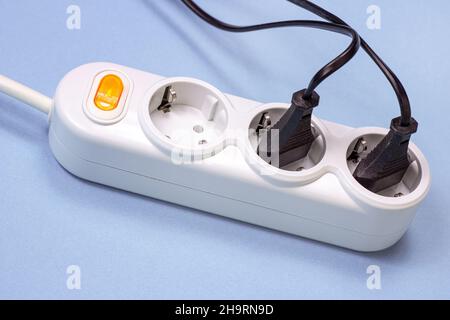 Triple socket white European power adapter with different wires at home. Standard electrical plug power outlet on blue background. Stock Photo