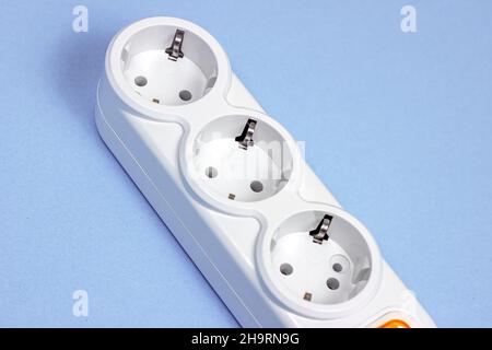 Triple socket white European power adapter with different wires at home. Standard electrical plug power outlet on blue background. Stock Photo