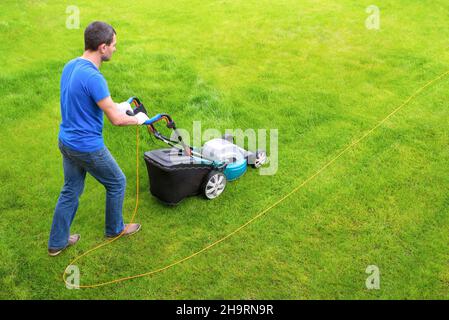 Gardener in the garden mows grass with a lawn mower. Side view. Stock Photo