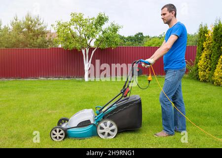 Worker with a lawn mower mows grass in the garden. Side view. Stock Photo