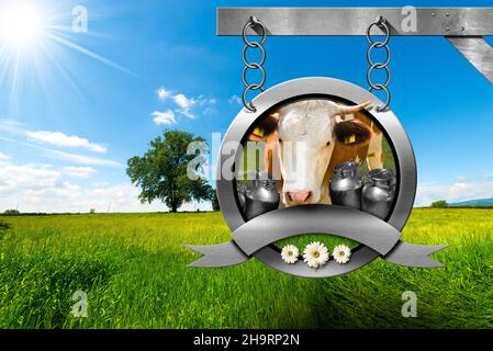 Dairy products sign with head of cow, milk canisters, green grass and daisy flowers. Hanging from a metal chain on a pole in a rural scene. Stock Photo