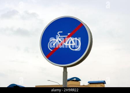 Blue and white bicycle lane sign with red forbid line indicating the end of the bike route, large round roadside traffic signage. Stock Photo