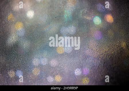 Abstract blur background with colourful bokeh behind a glass with water drops. defocused glitter lights in darkness. Night magic of new year. Artistic Stock Photo