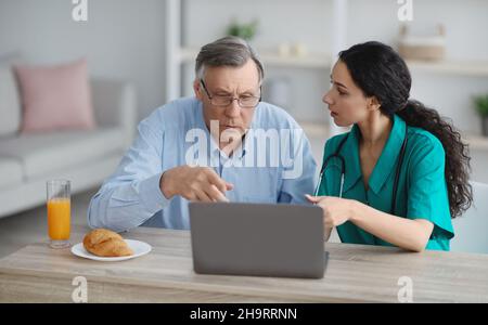 Young nurse showing senior man in wheelchair how to use laptop at retirement home Stock Photo