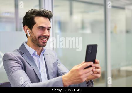 Successful young business man using smartphone and headset during a video conference Stock Photo