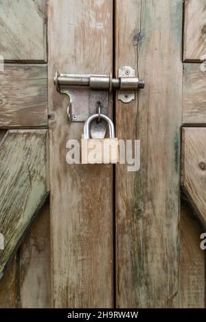 one closed padlock on the pin of a rustic wooden door, metal object texture, concept of locked entry and security, background Stock Photo