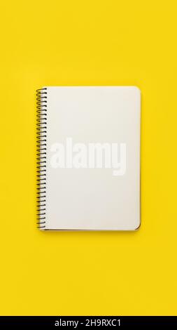 Open spiral notebook with blank empty white sheets and binder on bright yellow background, top view, flat lay Stock Photo