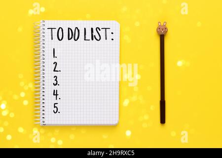 Open spiral squared notebook with to do list and brown pen with bunny head on bright yellow background with blurred lights bokeh, top view, flat lay Stock Photo