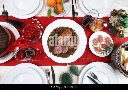 Traditional Italian Christmas food.   Cotechino with lentils, appetizer, fruits, red wine and Panettone. Family gathering concept. Directly above. Stock Photo