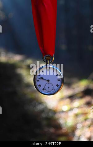 old silver pocket watch hanging from a red ribbon with abstract background. Stock Photo
