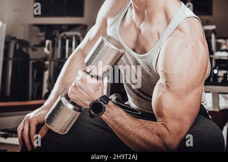 Muscular man working out in gym doing exercises with dumbbells at biceps Close up Stock Photo